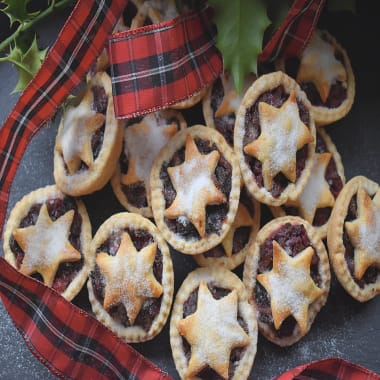 Cranberry Tarts on a black board with tartan ribbon and holly decorations.